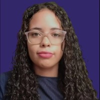 Mulher de cabelo castanho cacheado, óculos rosa, usando uma camiseta azul escuro